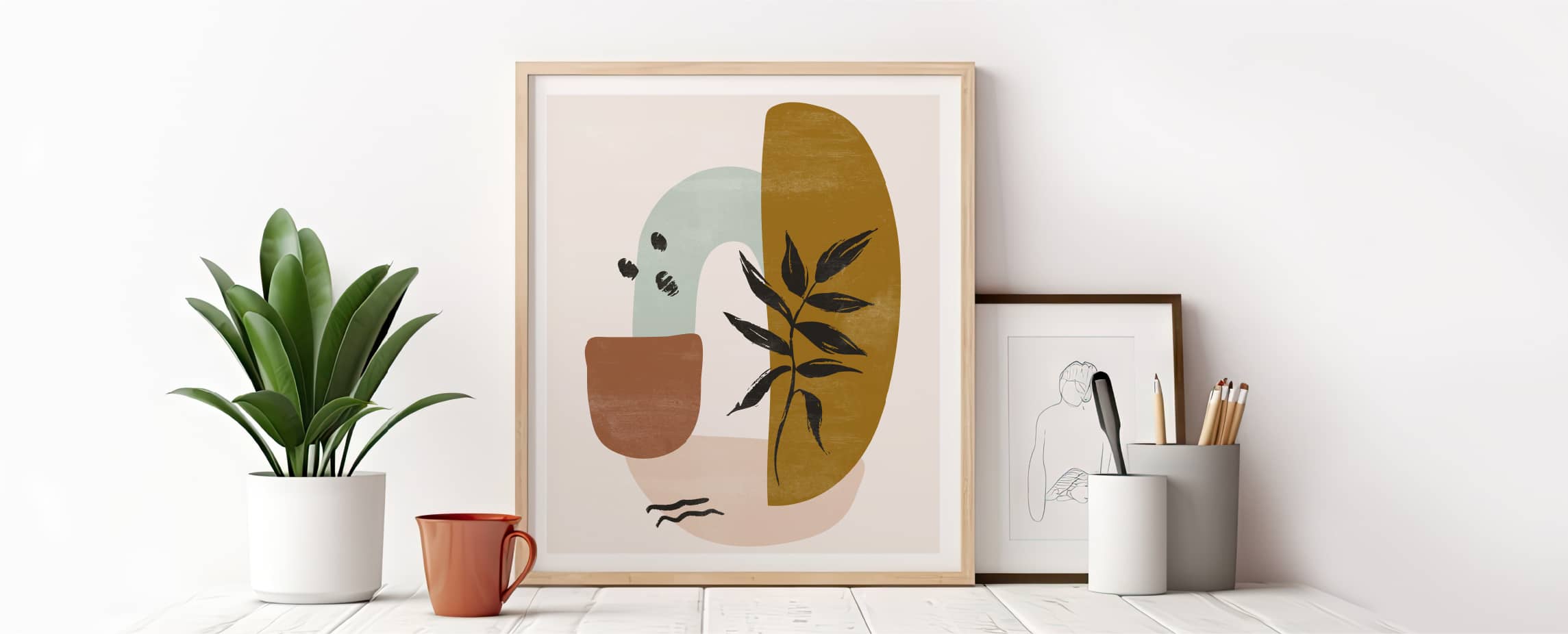 Geometric modern art framed surrounded by a framed abstract artwork, potted plant, and cup of pencils.